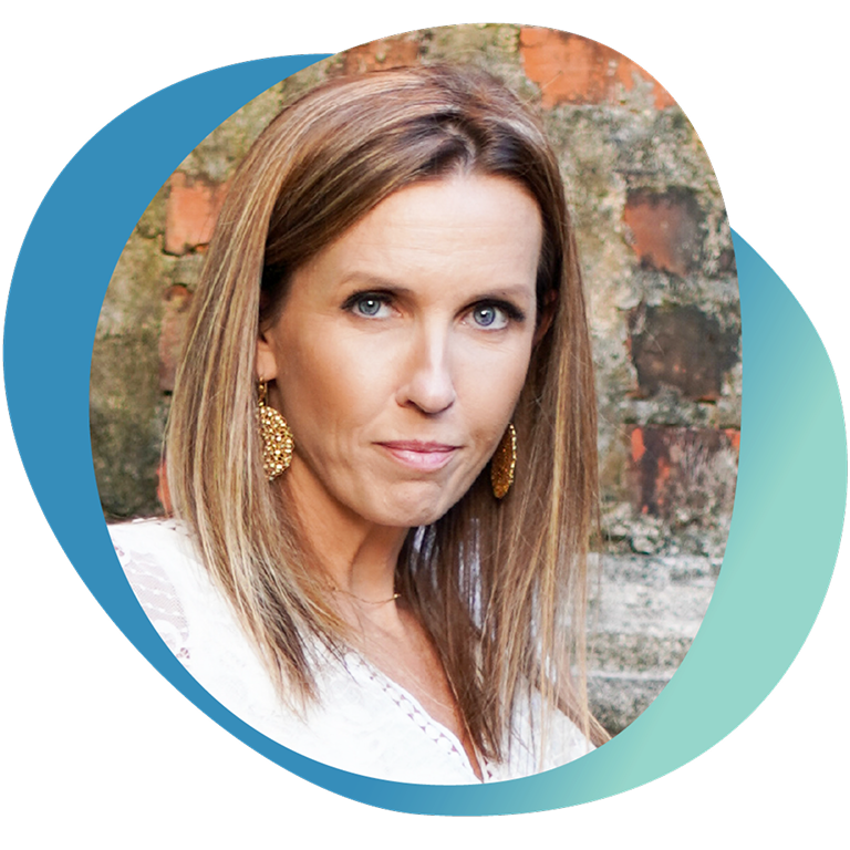 Portrait of Heather with long straight hair and gold earrings, standing in front of a brick wall