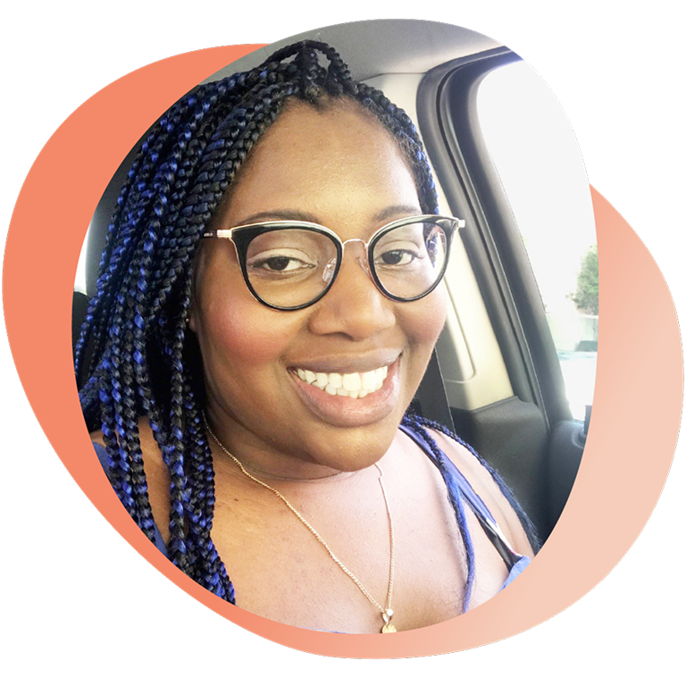 Portrait of Mary smiling while seated in a car, wearing glasses and a necklace